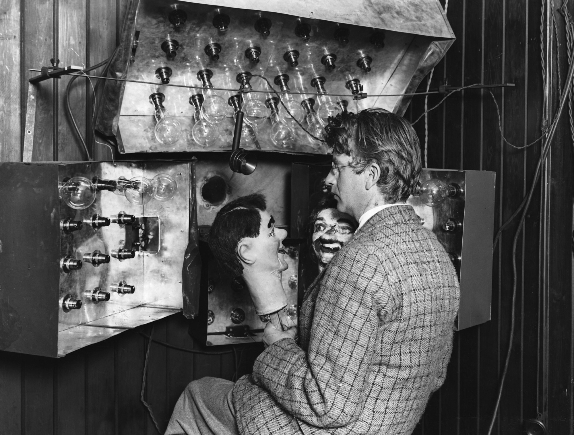 John Logie Baird beside his apparatus, holding a ventriloquist's dummy used in early television experiments.